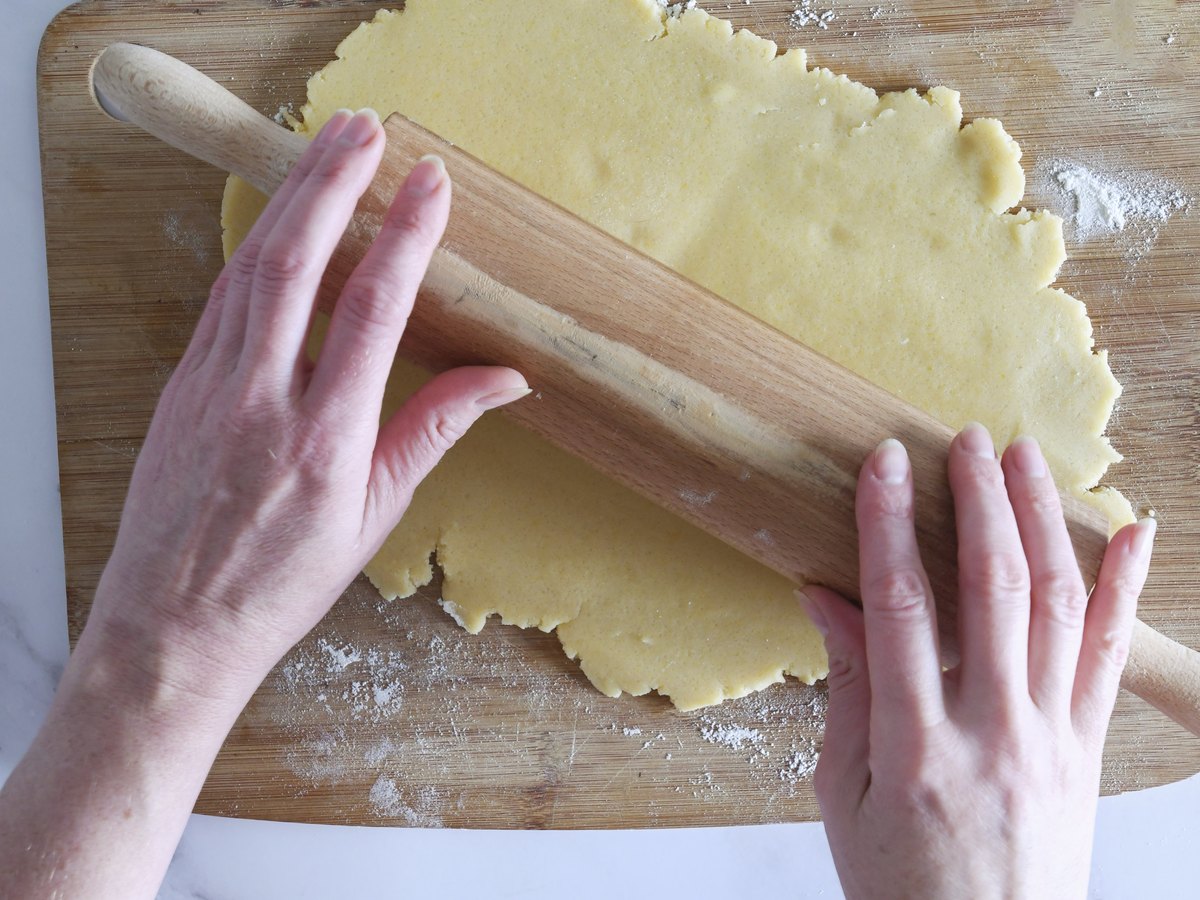 Mürbeteig wird mit einem Holzrollholz ausgerollt