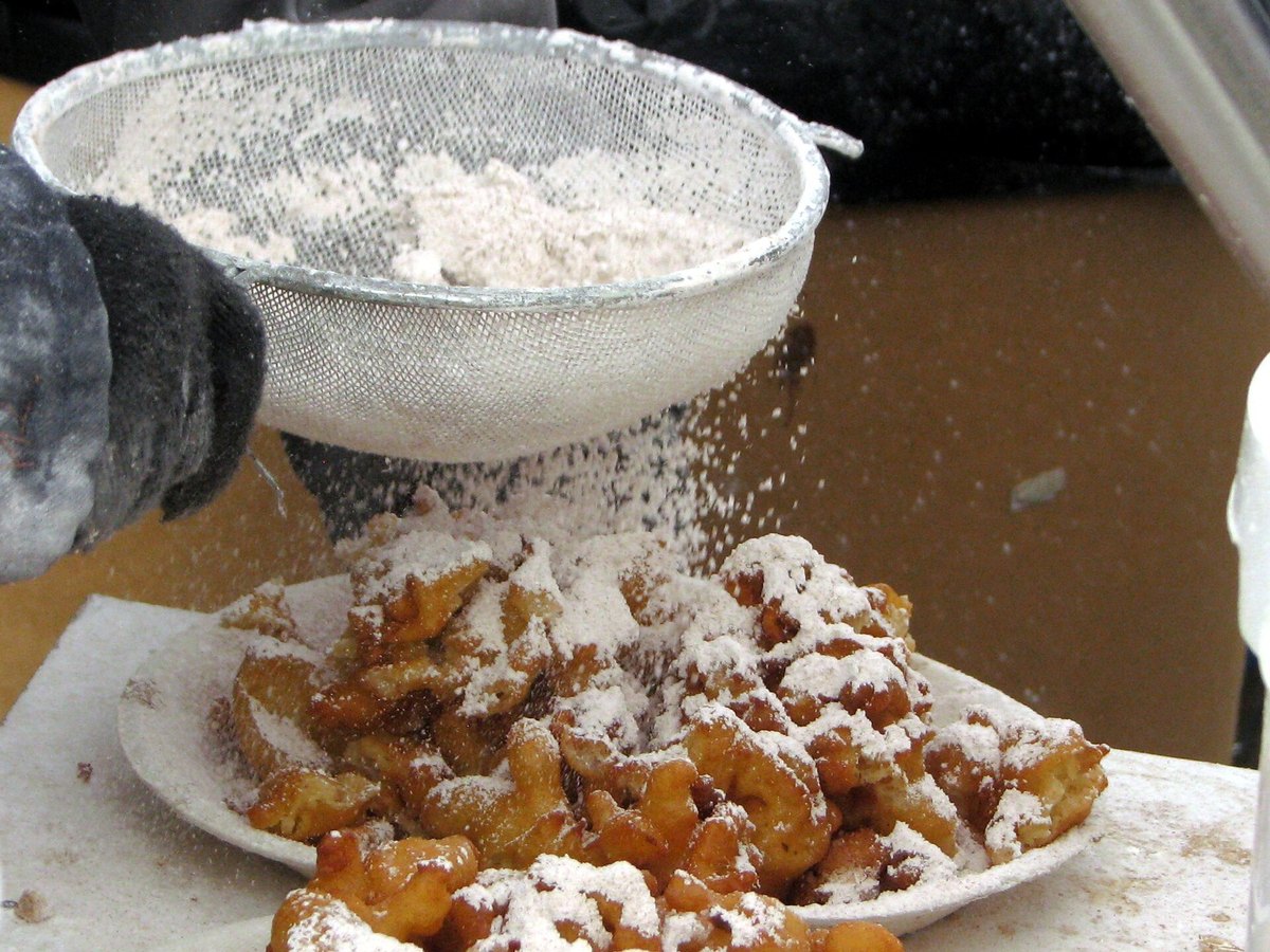 Puderzucker wird über frisch gebackenes Schmalzgebäck gesiebt