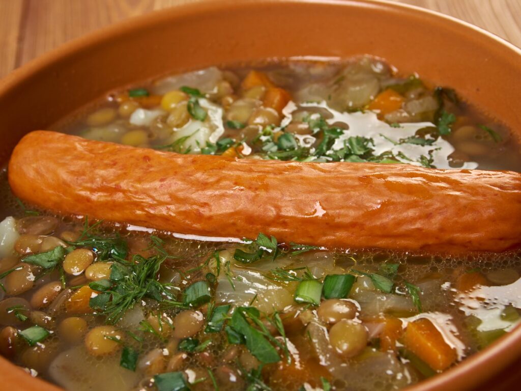 Topf mit klassischer Linsensuppe, dazu ein Würstchen und frische Petersilie