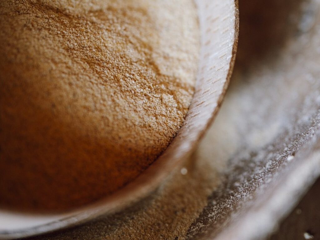 Corn flour being sifted in a wooden bowl used for baking on a kitchen counter