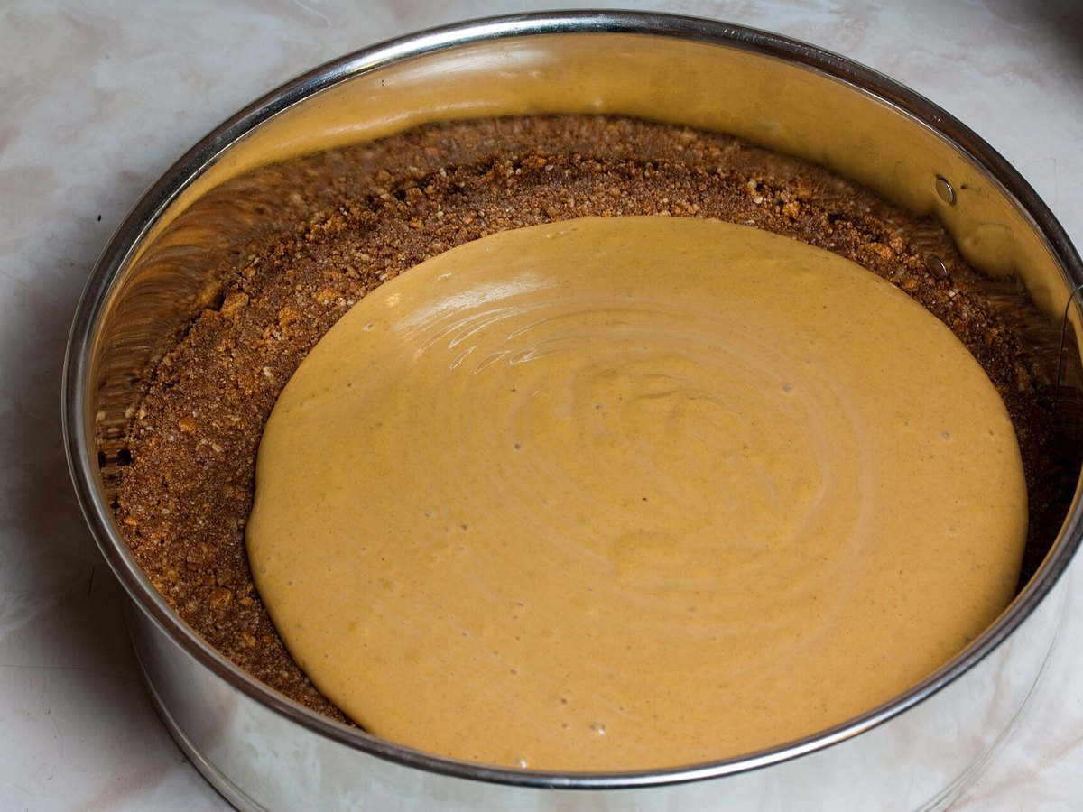 Cremige Käsekuchen-Masse liegt auf dem Keksboden in der Springform